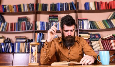 Adam meşgul yüz kitap okumak, kitap rafı arka plan üzerinde. Eğitim ve bilim kavramı. Öğretmen ya da sakal Kitaplığı'nda eğitim ile öğrenci. Bilim adamı okuma, kupa ve kum saati ile masada oturur