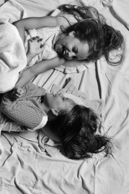 Çocuklar mutlu yüzler ile yatakta dinlenin. Beyaz ve pembe yatak çarşafları arka plan gıdıklıyor kızlar yalan söyler