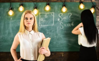 Öğrenci ve kursiyer kavramı. Kız defocused kara tahta arka plan üzerinde yazma Bayan ise kendinden emin görünüyor. Portre portre çekici genç kadın, öğrenci holding kitap sınıf