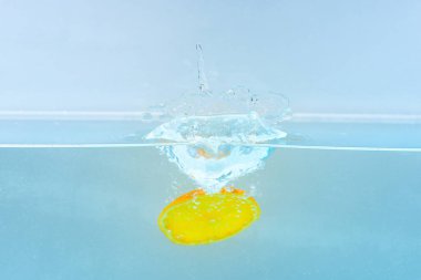 Turuncu şeffaf kabarcıklar ve su ile su altında dilim sıçramalarına bırakır. Saf, şeffaf sıvı turuncu. Meyve suyu, mavi arka plan düşmek. Kokteyl yapma kavramı