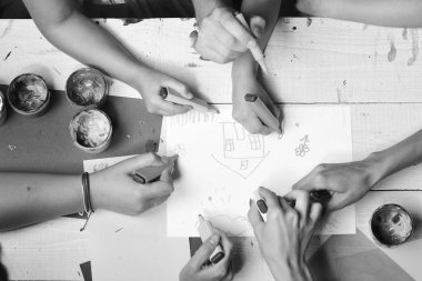 Sanatçı ahşap masa boyalar ve renkli kağıt ile. Elele tutuşun renkli işaretleyicileri ve beraberlik, üstten görünüm. Sanat ve fikir kavramı. İşaretleri erkek ve kadın elinde çizimleri ile beyaz kağıt üzerinde çizmek.