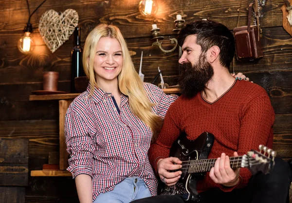 Romantic evening concept. Couple in wooden vintage interior enjoy guitar music. Lady and man with beard on happy faces hugs and plays guitar. Couple in love spend romantic evening in warm atmosphere