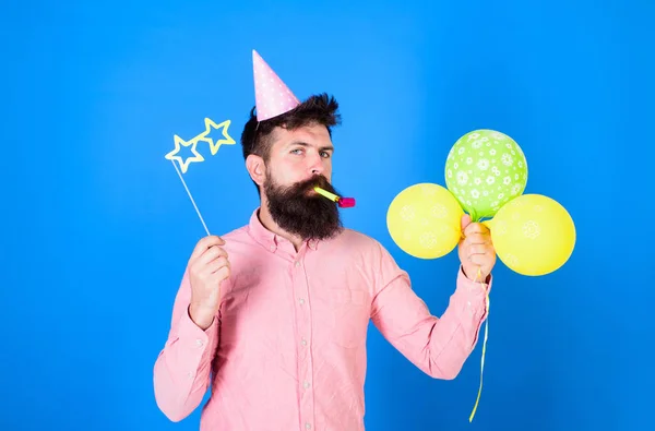 Bearded party entertainer at kids celebration, International children day concept. Man with bright balloons, paper glasses and cap at birthday party. Bearded hipster in pink shirt on blue background