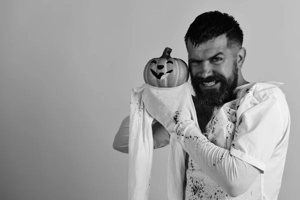 Man with evil smile on yellow background, copy space. Guy with beard holds smiling orange pumpkin. Halloween character