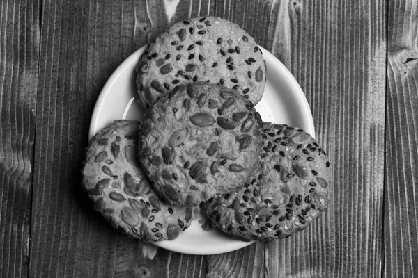 Bisküvi plaka üzerine yerleştirilen tohumları ile kapatın. Ahşap arka plan üzerinde yulaf ezmesi kurabiye yapılmış