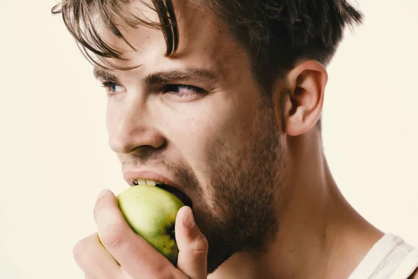 Um tipo com cara séria, isolado no fundo cinzento claro, de perto. O homem com maçã verde na mão morde-a. Atleta com cabelo bagunçado come frutas frescas. Nutrição e saúde — Fotografia de Stock