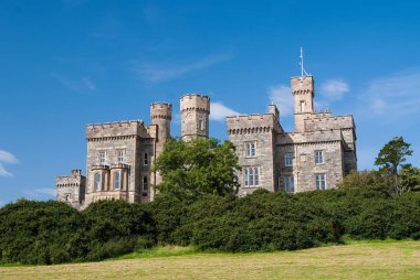 Lews Castle on blue sky in Stornoway, United Kingdom. Castle with green trees on natural landscape. Victorian style architecture and design. Landmark and attraction. Summer vacation and wanderlust clipart