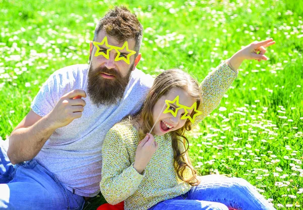 Rock ster concept. Familie doorbrengen vrijetijdsbesteding buitenshuis. Vader en dochter zit op gras op grassplot, groene achtergrond. Kind en vader poseren met ster vormige eyeglases foto stand kenmerk op weide — Stockfoto