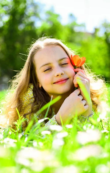 Barn njuta av soliga vårdag liggandes på ängen. Flicka på drömmande ansikte innehar röd tulip flower, Njut doften. Säsongsbunden allergi koncept. Flicka liggande på gräset, naturen på bakgrund, oskärpa — Stockfoto