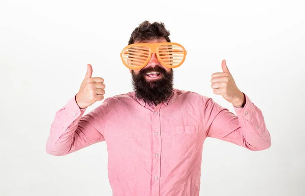 Concetto allegro di umore. Hipster che guarda attraverso gli occhiali da sole giganti a strisce. Il tizio con la barba mostra i pollici in su. Uomo con barba e baffi sul viso felice indossa occhiali grandi divertenti, sfondo bianco — Foto Stock