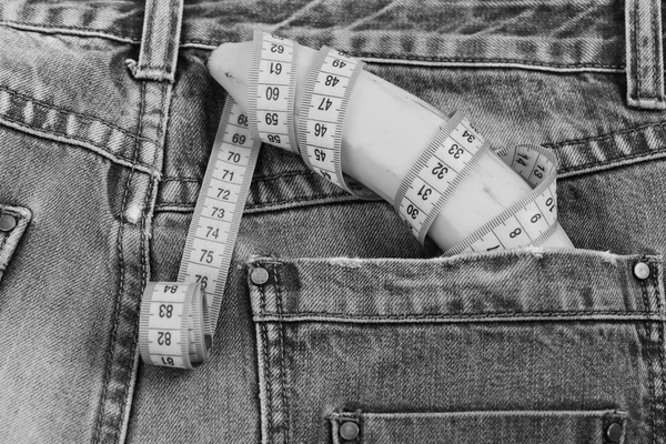 Banana wrapped with yellow measure tape sticking out from jeans pocket. Mens denim pants with banana imitating male genitals — Stock Photo, Image