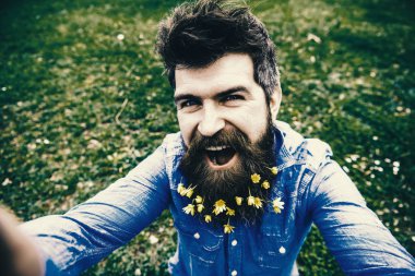 Doğal güzellik kavramı. Hippi mutlu yüz selfie fotoğraf çekiyorum. Sakallı bahar, yeşil çayır arka plan, defocused sahiptir. Selfie fotoğrafta sakallı küçük kırlangıçotu çiçekli adam