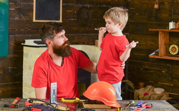 Yürümeye başlayan araçlar ve kask ile ev atölye sakallı babasıyla. Babalık kavramı. Çocuk çocuk babası ile eğlence keyfini çıkarın. Baba ve oğul birlikte onarımı veya handcrafting süre vakit.