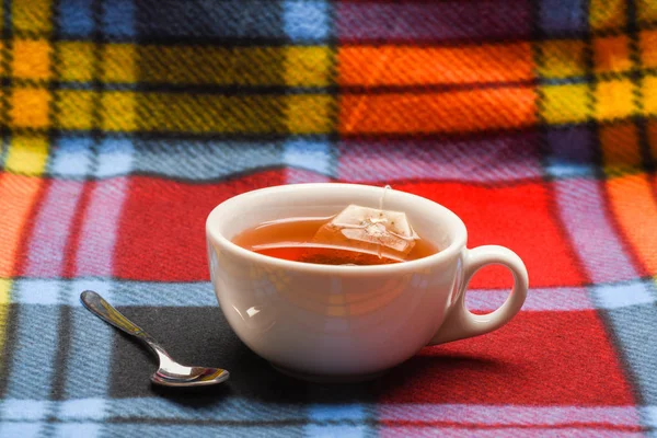杯子里装满了热水和蘸着的茶叶。茶酿造理念。杯子里装满了沸水, 泡茶和勺子上五颜六色的格子背景。陶瓷杯茶酿造工艺的研究 — 图库照片