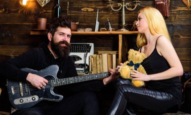 Gitar çalmak ve evde oturan bir çift. Relax tatil kavramı. Adam oyun gitar Bayan ise oyuncak ayı elinde tutar. Çift Romantik akşam, ahşap iç arka plan geçirmek