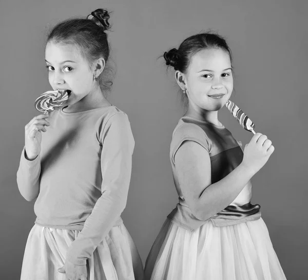 Schwestern mit runden und lang geformten Lutschern. Kinder mit glücklichen Gesichtern posieren mit Bonbons auf grünem Hintergrund. — Stockfoto