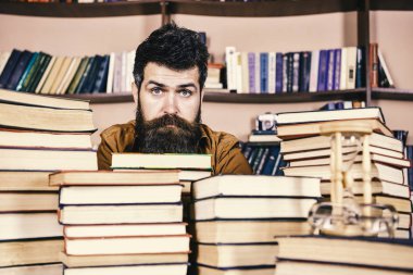 Kitaplığı'nda, eğitim sırasında kitaplar, kitap rafı arka plan üzerinde yığınları arasında sakin yüz kişi. Kazık kavramı. Öğretmen ya da öğrenci sakallı defocused kitaplar ile masada oturur