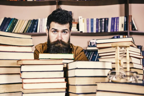 Kitaplığı'nda, eğitim sırasında kitaplar, kitap rafı arka plan üzerinde yığınları arasında sakin yüz kişi. Kazık kavramı. Öğretmen ya da öğrenci sakallı defocused kitaplar ile masada oturur