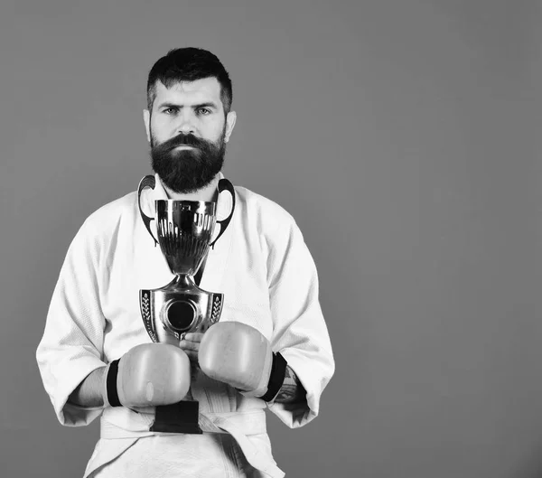 Καράτε άνθρωπος με σοβαρό πρόσωπο σε γάντια πυγμαχίας κατέχει κύπελλο — Φωτογραφία Αρχείου