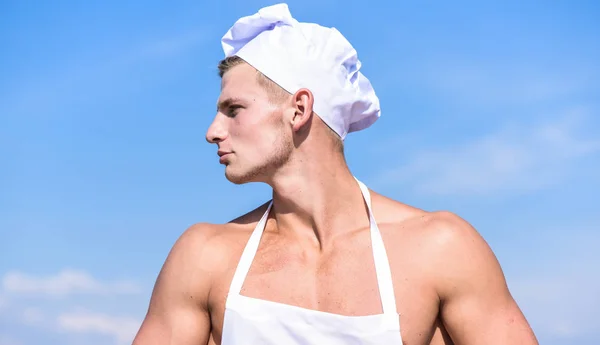 Man op vertrouwen gezicht draagt koken hoed en schort, sky op achtergrond. Cook of chef-kok met gespierde schouders en borst ziet er aantrekkelijk uit. Chef-kok met naakt sexy gespierd torso. Mannelijkheid concept — Stockfoto