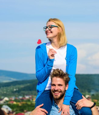 Adam kız arkadaşı omuzlarında, gökyüzü arka plan taşır. Romantik tarih kavramı. Kadın kalp aşk sopa sembolü üzerinde tutar. İki açık güneşli gün yürüyüş seviyorum. Çift mutlu Tarih birlikte eğleniyor