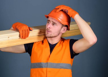 Adam kask, kask ve koruyucu eldiven tutan ahşap kiriş, gri arka plan. Güvenlik ve koruma kavramı. Marangoz, woodworker, ciddi bir yüz taşıdığı ahşap kiriş omuz üzerinde güçlü Oluşturucu