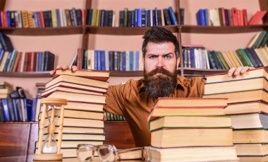 Öğretmen ya da öğrenci sakallı kum saati ve gözlük, defocused ile masaya otur. Katı yüz sit Kitaplığı'nda, eğitim sırasında kitaplar, kitap rafı arka plan üzerinde yığınları arasında adam. Kitap kurdu kavramı