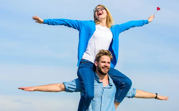 Freedom concept. Couple in love enjoy feeling freedom outdoor sunny day. Man carries girlfriend on shoulders, sky background. Lovers enjoy date and feeling free. Couple happy date having fun together