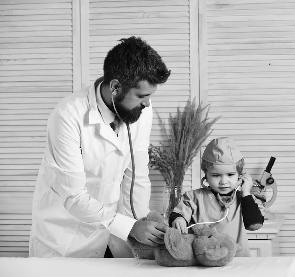 El veterinario y el ayudante examinan al oso de peluche. Padre e hijo con caras atentas jugando al doctor . — Foto de Stock