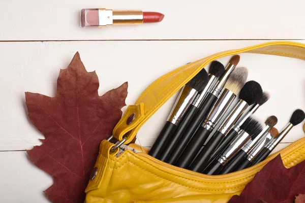 Makeup brushes inside bag near red autumn leaves