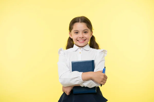 Jag är redo för skolan. En skoluniform, smart kille, klar med läxorna. Flicka söt glad ansikte gul bakgrund. Barnflicka skoluniform kläder håller bok och penna. Tillbaka till skolkonceptet — Stockfoto