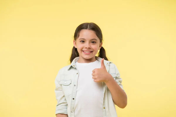 Jó minőség. A kislány hüvelykujját felfelé mutatva sárga hátteret javasol. A gyermek erősen ajánlom hüvelykujjával felfelé gesztus. Lány boldog mosolygós ajánlani kiváló minőségű termék. Döntsön helyesen. — Stock Fotó