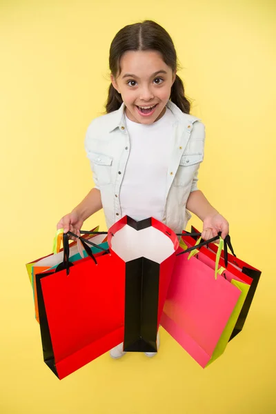 Ezt figyeld. Gyerek aranyos fashionista vásárlás. Gyerek lány boldog mosolygós arc hordoz csokor csomag sárga háttér. A lány boltos szeret vásárolni az akciós szezonban. Boldog bevásárlást a plázában. — Stock Fotó
