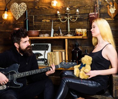 Romantik tarih kavramı. Rahat yüzleri aşık çift romantik atmosferinin keyfini çıkarın. Adam oyun gitar Bayan ise oyuncak ayı elinde tutar. Çift Romantik akşam, ahşap iç arka plan geçirmek