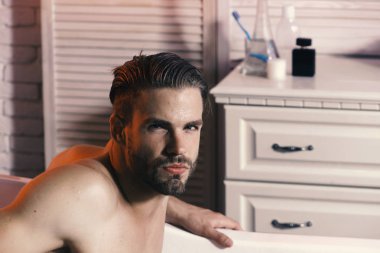 Sakal ve baştan çıkarıcı yüz ifadesi olan adam. Adam banyoda tuvalet malzemeleri bulunan arka plan üzerinde.