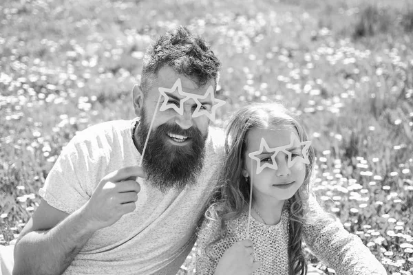 Ребенок и папа позируют со звёздными очками атрибут фотобудки на лугу. Отец и дочь сидят на траве на зеленом фоне. Суперзвезда концепция. Семья проводит досуг на открытом воздухе — стоковое фото