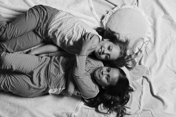 Pajama party and childhood concept. Girls lie on white and pink bed sheets hugging — Stock Photo, Image