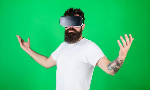 Koncepcja wyższości. Hipster na poważnej twarzy podnosi ręce, ciesząc się wyższością w wirtualnej rzeczywistości. Facet z wyświetlaczem montowanym na głowie wchodzi w interakcję w VR. Mężczyzna z brodą w okularach VR, zielone tło — Zdjęcie stockowe
