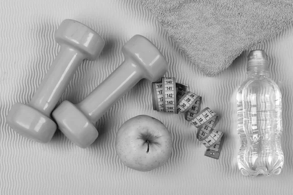 Dumbbells made of plastic on wavy green texture background, top view. Barbells, apple and water bottle near blue measuring tape