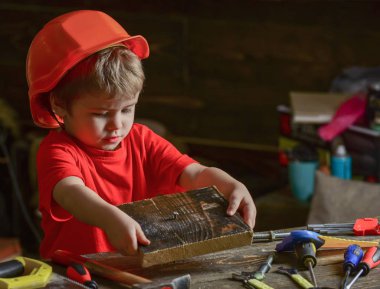 Kask Oluşturucu veya repairer, onarımı veya handcrafting olarak oynayan sevimli çocuk. Kavram handcrafting. Çocuk kör kütük çocuk tırnak ahşap pano içine. Yürümeye başlayan çocuk meşgul yüz oyunlarında evde atölye üzerinde
