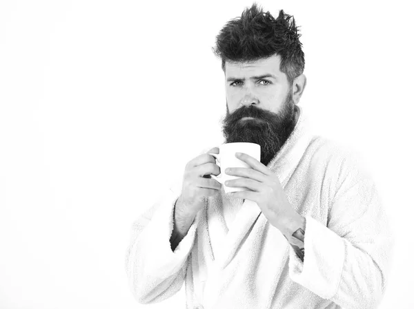 Concept de rituels matinaux. Macho somnolent avec le visage strict boit du café le matin, l'espace de copie. Homme barbe et cheveux ébouriffés en peignoir, tient une tasse avec thé ou café, fond blanc — Photo