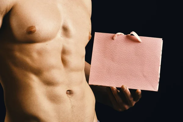 Corps d'athlète en gros plan, main tenant sac à provisions texturé rose. Homme avec torse nu isolé sur fond noir — Photo