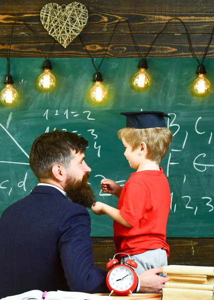 神童儿童概念。老师带着胡子, 父亲在教室里教小儿子, 黑板上的背景。男孩, 孩子在研究生盖帽讨论黑板上的涂鸦, 而教师听 — 图库照片