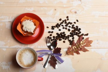 Yazılı kelime kahve ile yaprak. Seramik sofra kahve, en iyi manzaralı. Cappuccino kahve sonbahar ahşap zemin üzerine bırakır, kahve çekirdekleri, cupcake, kaşık ve çatal. Kahve saati kavramı