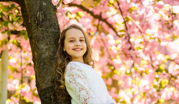Sakura, Ağaç gövdesinde yalın yakın duran yüz gülümseyerek kıza. Uzun saçları açık, kiraz çiçeği veya sakura çiçek arka plan üzerinde olan kız. Şirin çocuk doğa bahar sabahı keyfini çıkarın. Bahar ruh kavramı