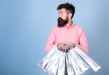 Uzun sakallı içinbeklediğini pembe tişörtlü adam. Alışveriş yaparken trendy sakallı hippi. Sakallı adam ile mavi arka plan., moda kavramı izole elinde gümüş alışveriş torbaları demet