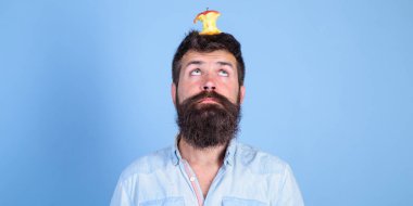 Canlı hedef kavramı. Adam yakışıklı hipster uzun sakal neredeyse kafasına elma güdük hedef olarak yem. Kilo kaybı gol. Hipster yüz elma güdük hedef üzerinde kafa mavi arka plan, kopya alanı ile şaşırttı