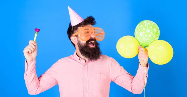 Чоловік з бородою і вусами на щасливому обличчі тримає повітряні кульки, синій фон. Хлопець у вечірньому капелюсі з святковими атрибутами святкує. Хіпстер у гігантських окулярах, що святкують день народження. Концепція партії — стокове фото