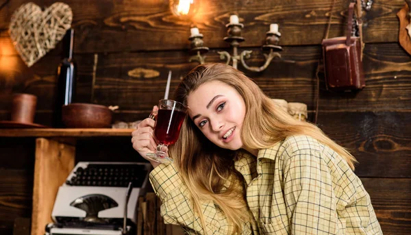 Girl tomboy relax with glass with mulled wine in house of gamekeeper. Relax concept. Lady on happy face in plaid clothes looks cute and casual. Girl in casual outfit sits in wooden vintage interior