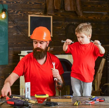 Evlat, çocuk neşeli cıvata veya vida, baba ile handcrafting sırasında eğlenmek tutar. Baba, ana okul atölyesinde farklı araçları kullanmak için kask öğretim oğlu sakallı. Tamirci kavramı.